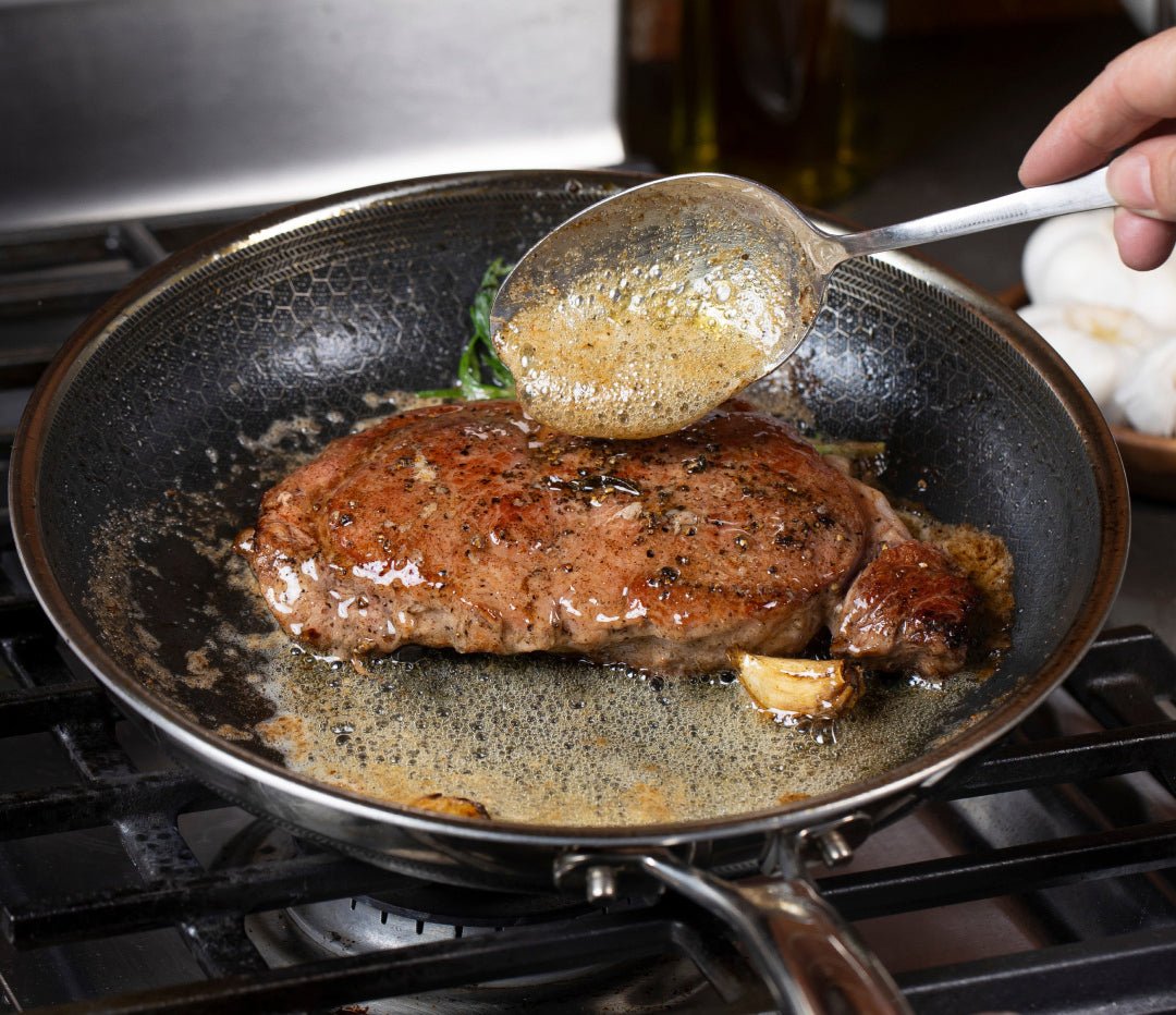 A steak being basted with butter in a pan on a stovetop.