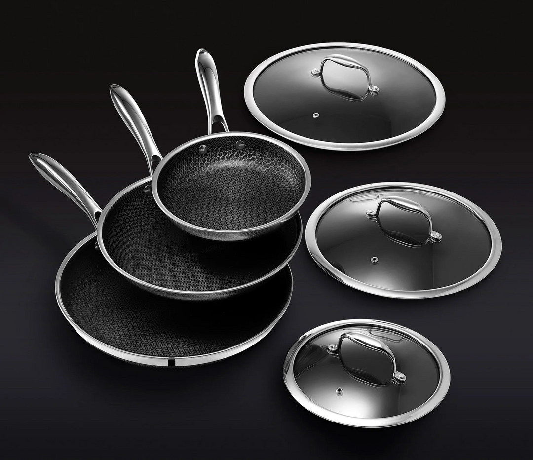 Stacked nonstick frying pans with matching glass lids on a black background.