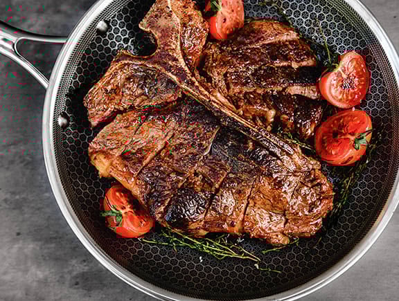 Grilled steaks with cherry tomatoes in a frying pan.