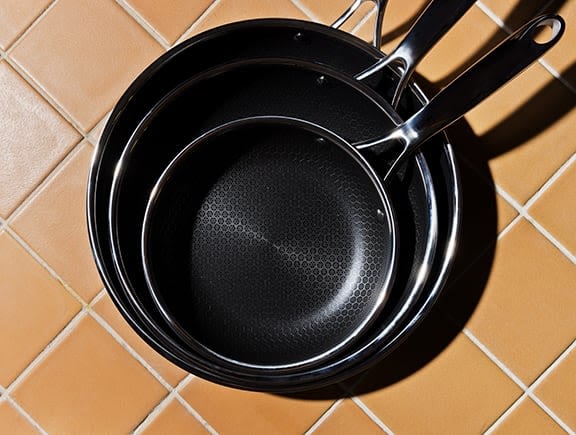 Stacked non-stick frying pans on a tiled kitchen counter.